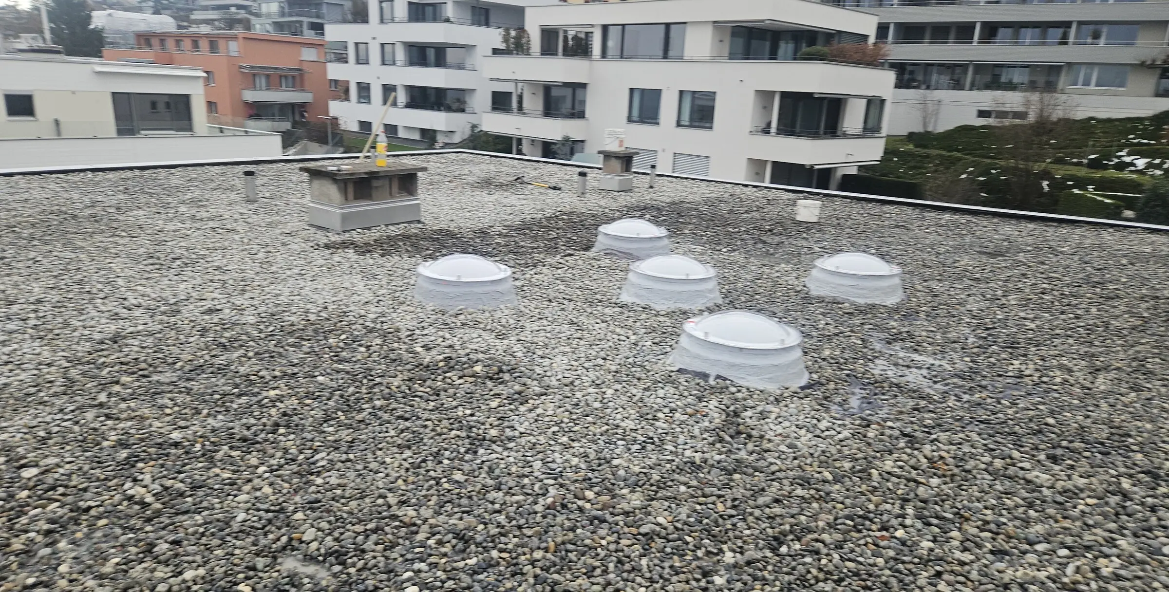 Weite Aufnahme eines Kiesdachs bei der jährlichen Kontrolle, Lichtkuppeln und Abläufe im Blick